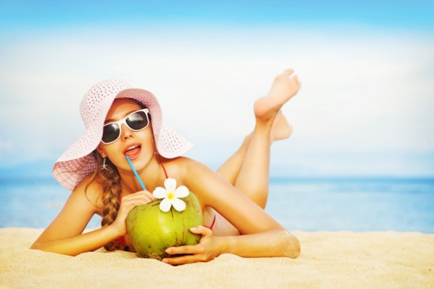 Young woman in pink swimsuit with coconut cocktail on the beach,