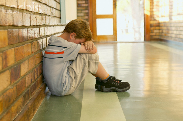 Sad schoolboy sitting in the hallway