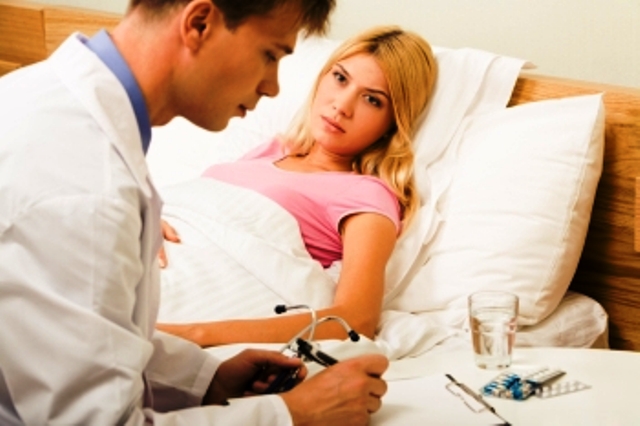 Sick female lying in bed and looking at male doctor while he prescribing her medication